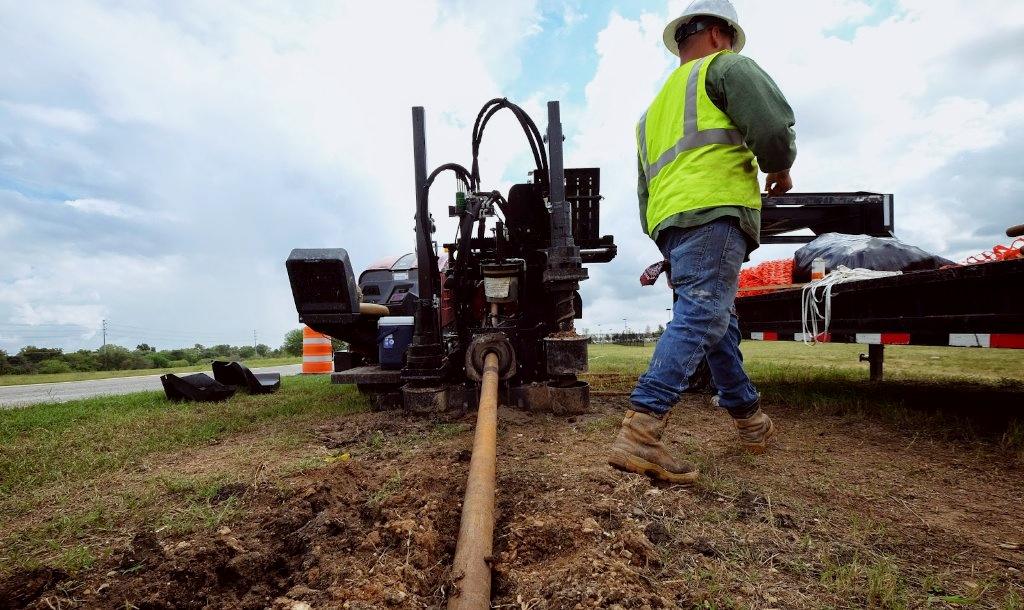 Crew member at a directional drill rig with pipe entering the ground